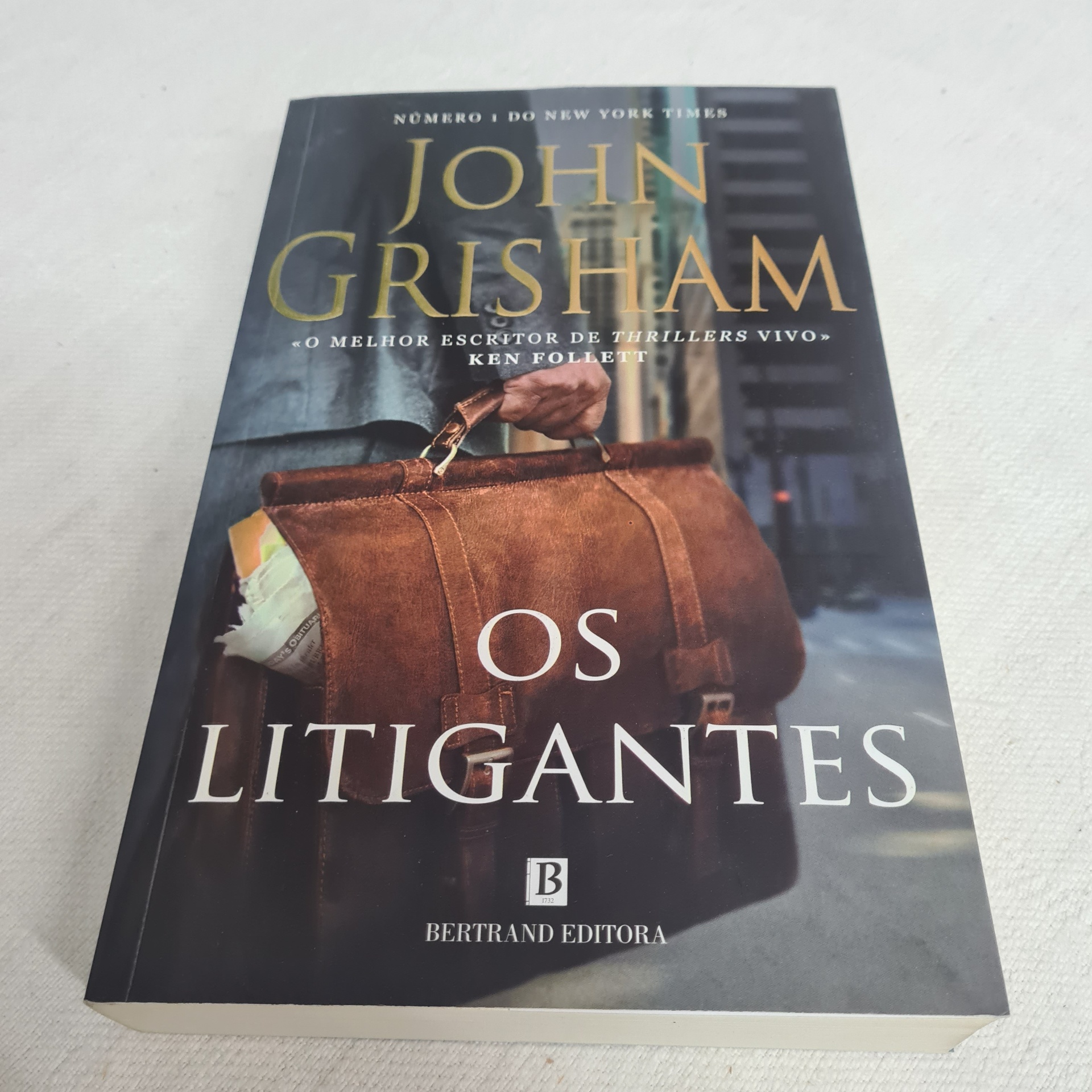 John Grisham - Os Litigantes Capa do livro 'Os Litigantes' de John Grisham com imagem de bolsa castanha de couro