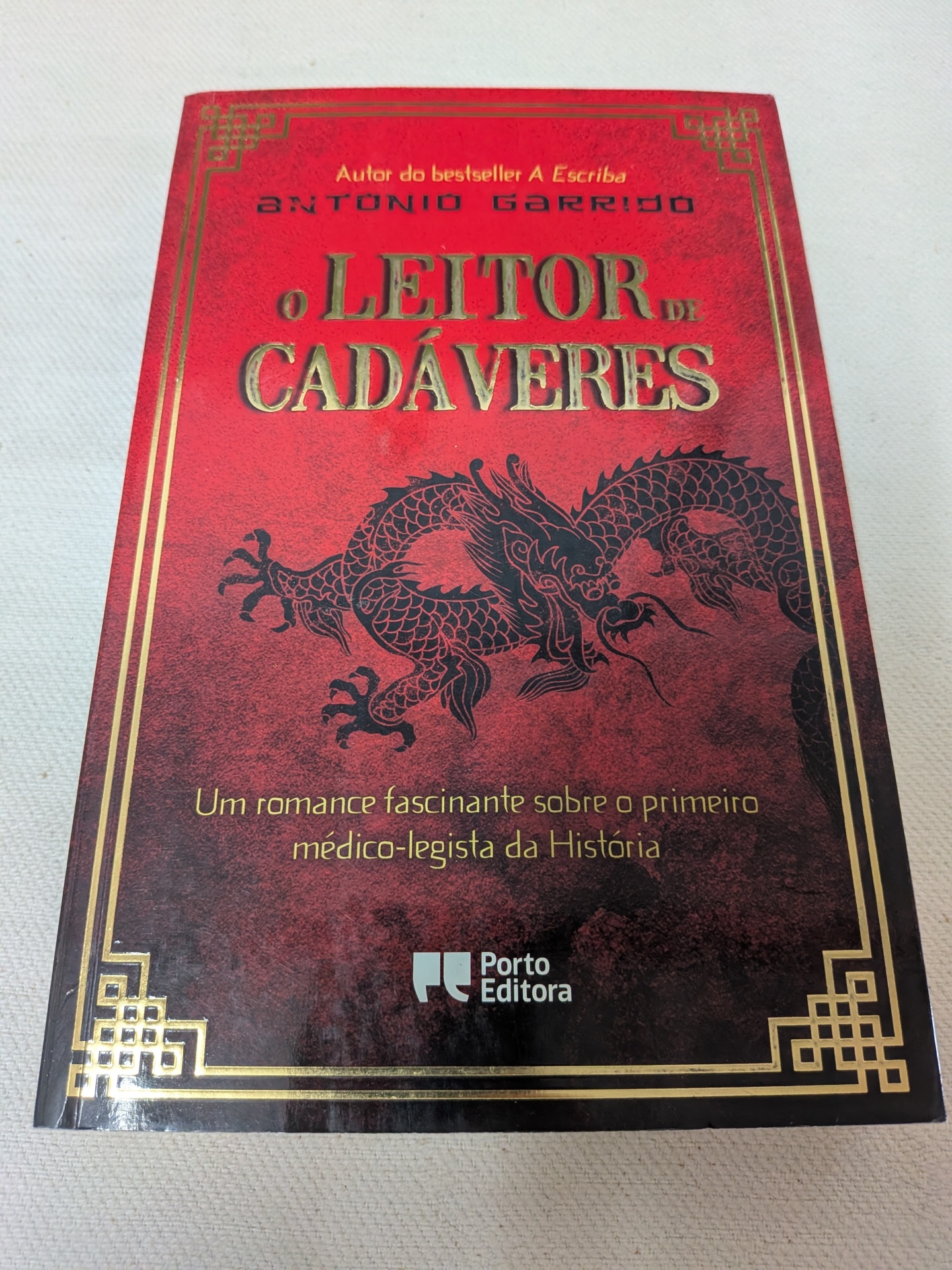Antonio Garrido - O Leitor de Cadáveres Capa vermelha de livro com dragão preto e texto dourado e amarelo