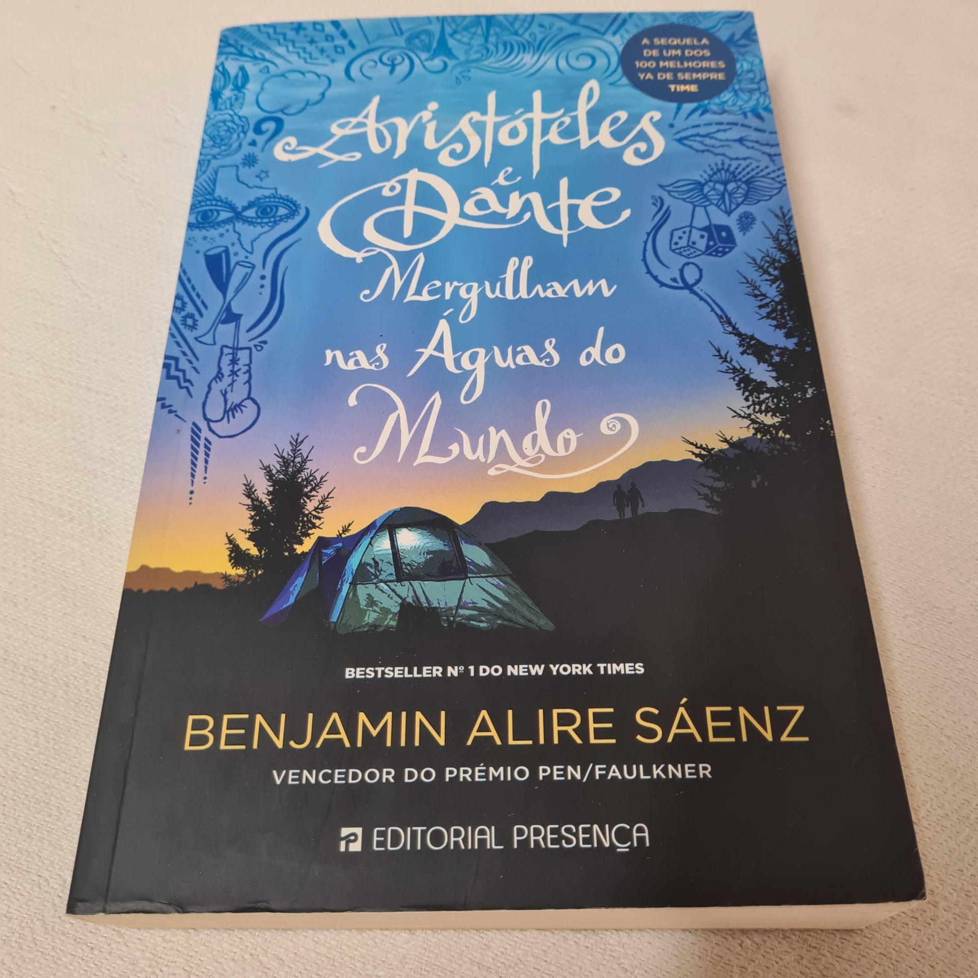 Benjamin Alire Sáenz - Aristóteles e Dante Mergulham nas Águas do Mundo Capa do livro 'Aristóteles e Dante Mergulham nas Águas do Mundo' com tenda azul e montanhas ao pôr do sol