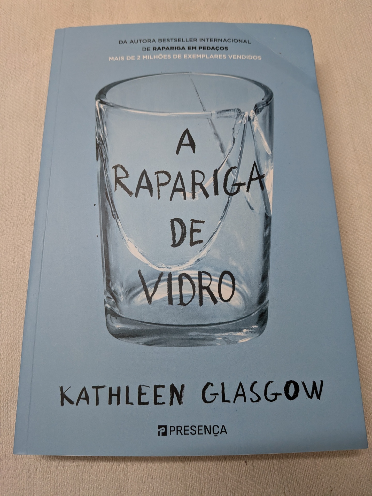 Kathleen Glasgow - A Rapariga de Vidro Capa de livro azul com copo de vidro partido e título A Rapariga de Vidro.