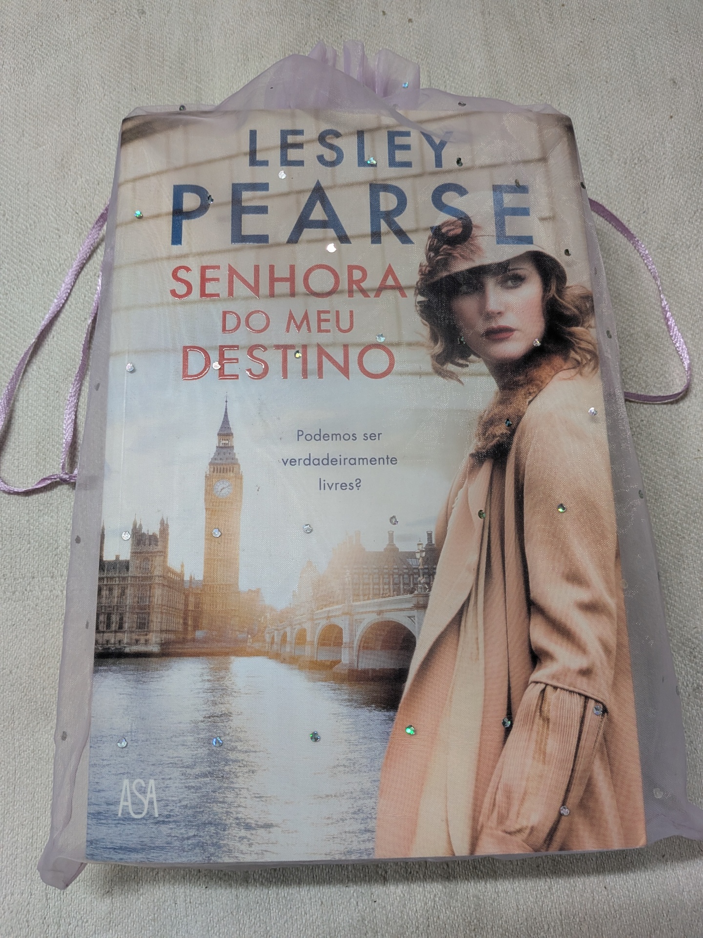 Lesley Pearse - Senhora do Meu Destino Saco lilás com bolso contendo livro Senhora do Meu Destino com capa que mostra Big Ben e mulher casaco bege.