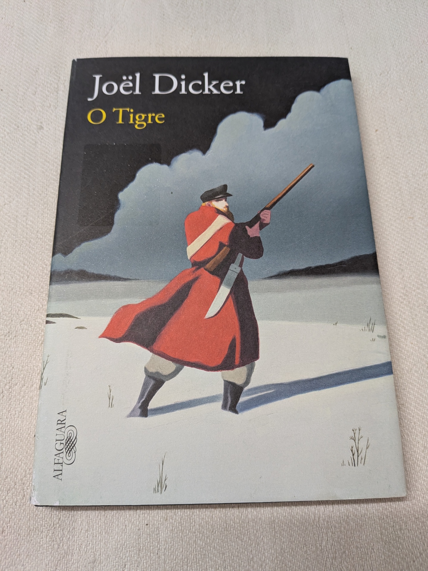 Joël Dicker - O Tigre Capa de livro com homem armado em paisagem nevada e o título Joël Dicker O Tigre.