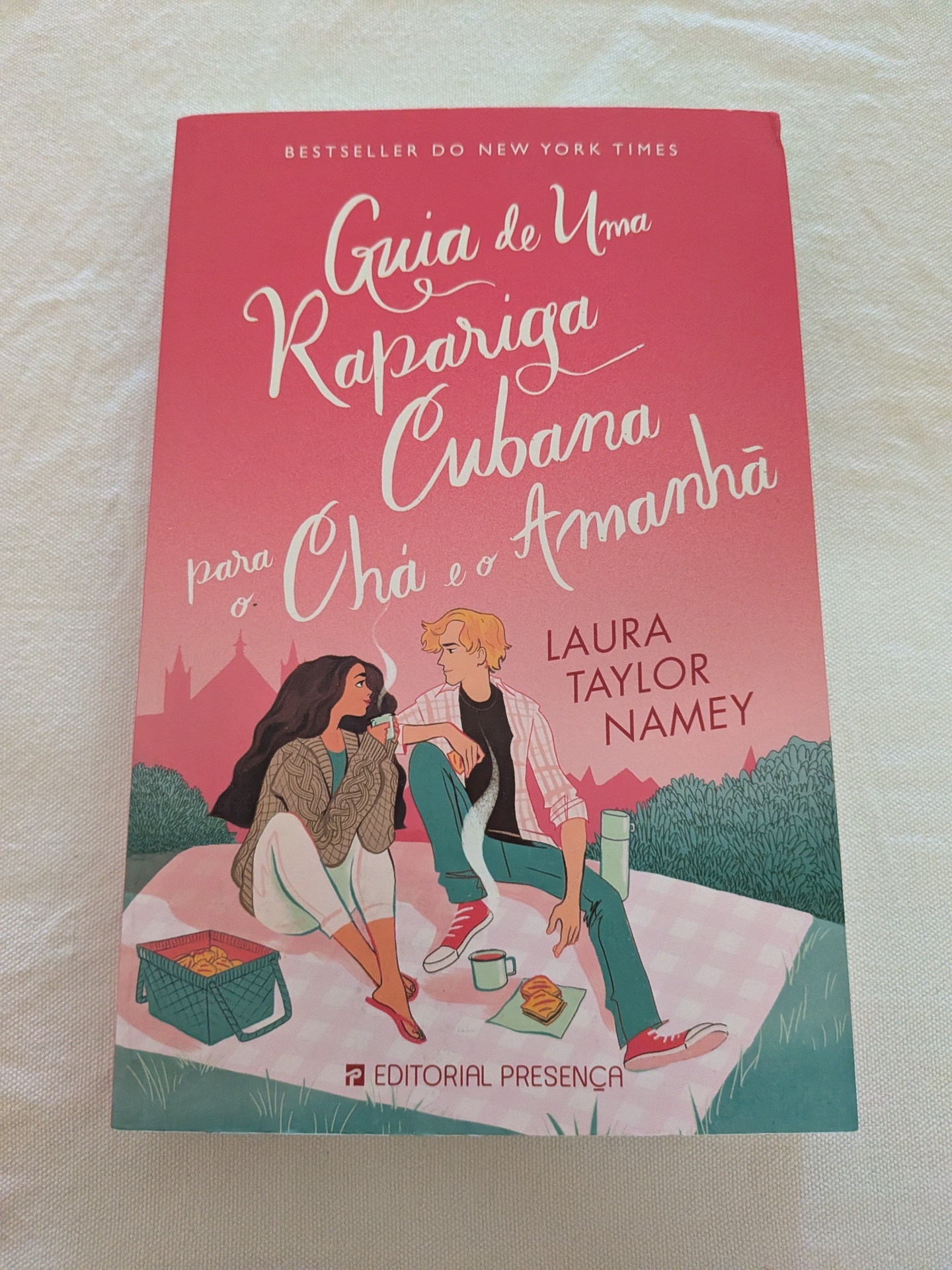 Laura Taylor Namey - Guia de Uma Rapariga Cubana para o Chá e o Amanhã Capa de livro em tons de rosa com ilustração de um casal num piquenique e texto informativo.
