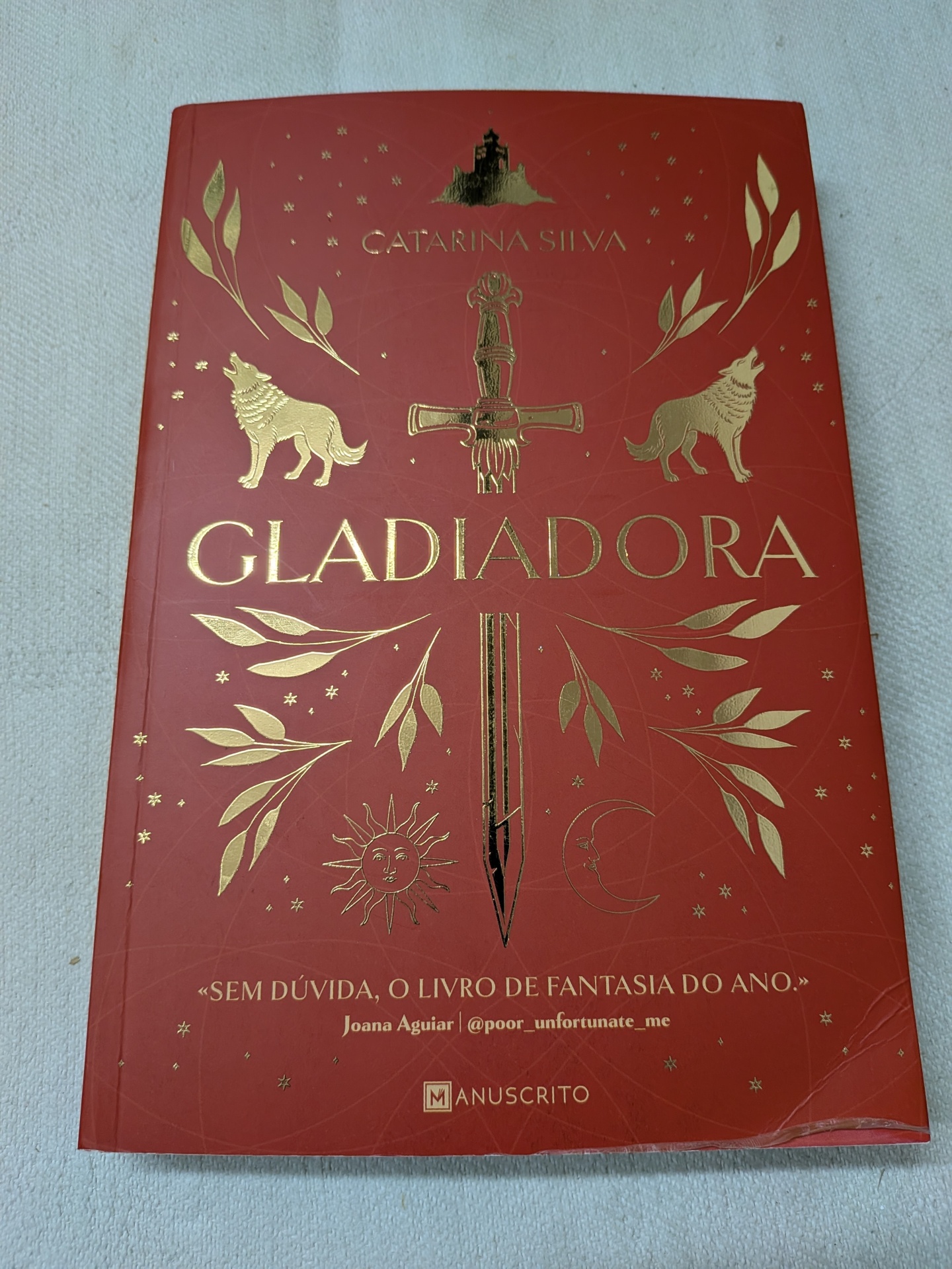 Catarina Silva - Gladiadora Capa de livro vermelha com texto e ilustrações douradas de espada, lobos, sol, lua e ramos