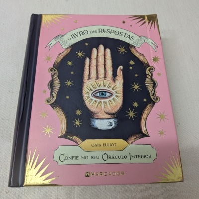 Livro com capa rosa, mão com olho azul e estrelas douradas