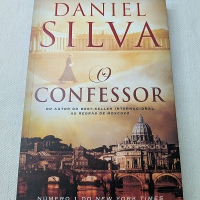 Capa do livro O Confessor com imagem de cidade histórica e padre caminhando
