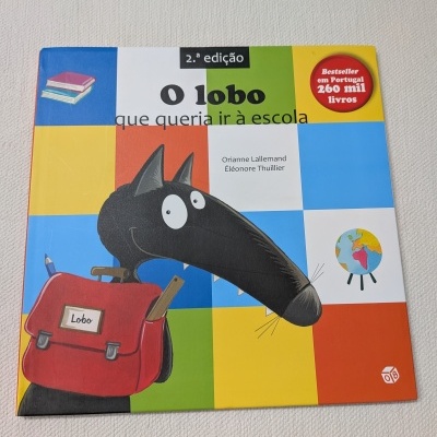 Capa de livro infantil colorida com desenho de lobo preto com mochila vermelha