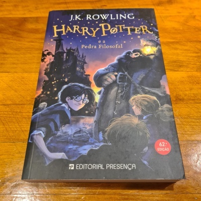 Capa do livro Harry Potter e a Pedra Filosofal, com ilustração de personagens e castelo, selo 62.ª EDIÇÃO