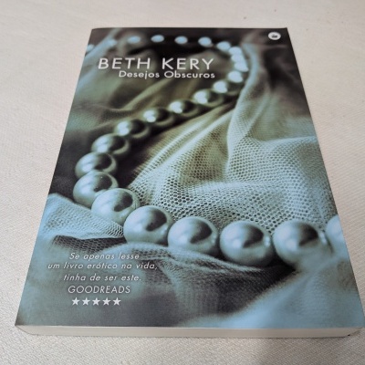 Livro 'Desejos Obscuros' com capa de colar de pérolas sobre tecido cinza