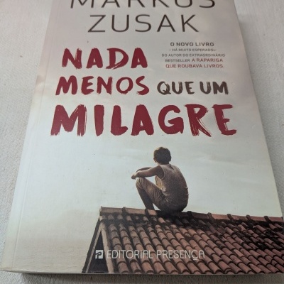 Capa do livro Nada Menos Que Um Milagre de Markus Zusak com imagem de menino sentado num telhado.