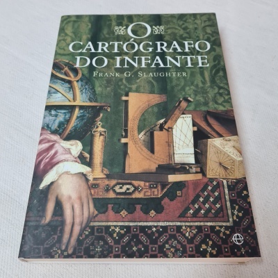 Livro O Cartógrafo do Infante com imagem de instrumentos cartográficos antigos sobre mesa com tapete