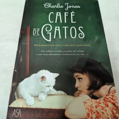 Capa de livro café de gatos com gato branco e mulher com boina