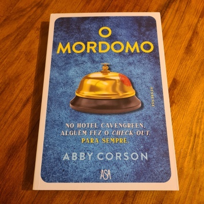 Capa de livro 'O MORDOMO' com campainha dourada e texto em azul, amarelo e branco