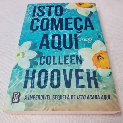 Capa do livro 'ISTO COMEÇA AQUI' de Colleen Hoover com flores e texto azul