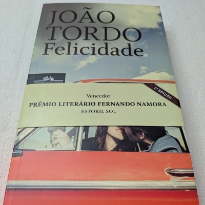 Livro Felicidade de João Tordo com imagem de casal num carro vermelho e faixa de prémio literário