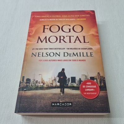 Livro Fogo Mortal de Nelson DeMille com capa laranja mostrando figura masculina e cidade ao fundo