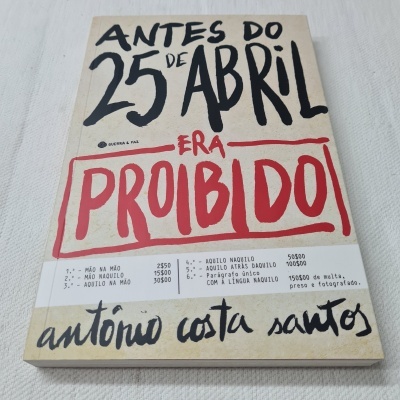 Capa de livro com texto em letras pretas e vermelhas e faixa branca com preços e autógrafo.