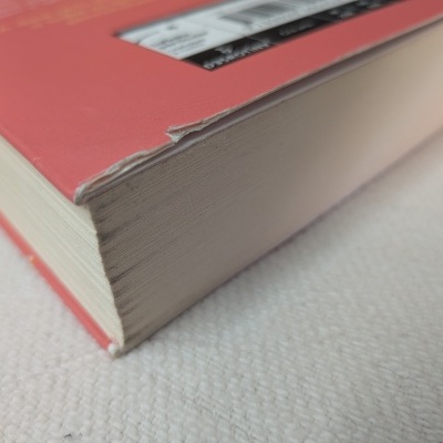 Livro capa dura rosa com canto danificado numa superfície branca