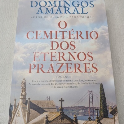 Capa de livro com túmulos, céu azul com nuvens e ponte ao fundo