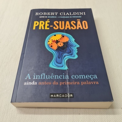 Livro 'Pré-suassão' de Robert Cialdini com ilustração de cabeça humana e engrenagens na capa azul.