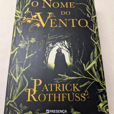 Capa do livro O Nome do Vento de Patrick Rothfuss com figura encapuzada envolvida por folhas verdes entrelaçadas.