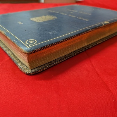 Livro antigo em capa de couro azul escuro com texto dourado num tecido vermelho