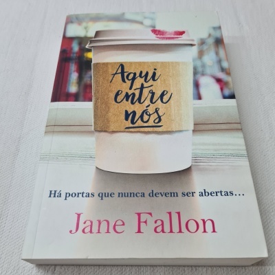 Capa do livro mostrando um copo de café com bandolete escrita 'Aqui entre nós'