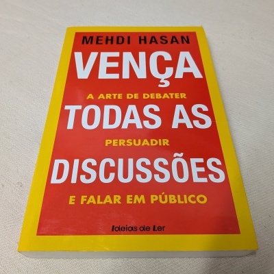Livro vermelho com moldura amarela e texto em branco e amarelo sobre mesa branca