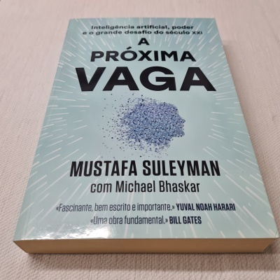 Livro 'A PRÓXIMA VAGA' de Mustafa Suleyman, capa azul clara com padrão e ilustração de cabeça humana feita de partículas azuis