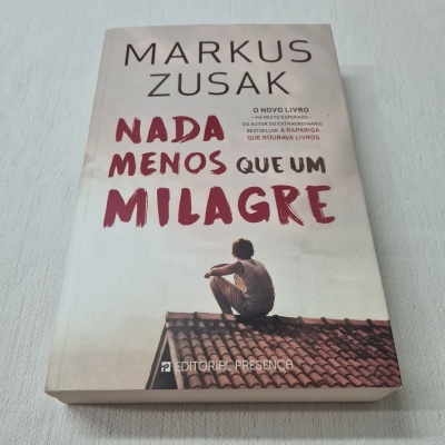 Capa do livro 'Nada Menos Que Um Milagre' de Markus Zusak com imagem de pessoa sentada no telhado.