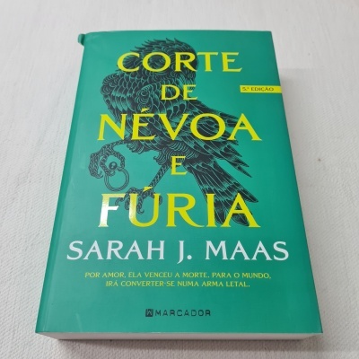 Livro 'Corte de Névoa e Fúria' com capa verde e ilustração de pássaro preto.
