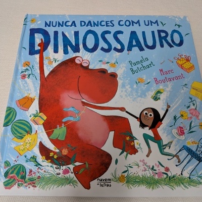 Capa azul de livro infantil com dinossauro vermelho e criança a dançar