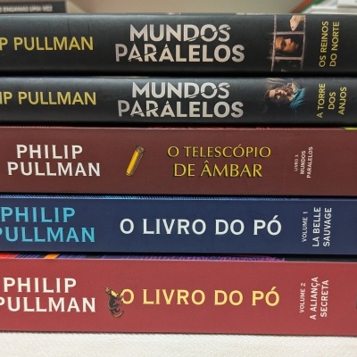 Empilhamento de livros de Philip Pullman com capas coloridas e números nas lombadas.