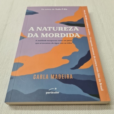 Capa do livro A Natureza da Mordida de Carla Madeira com design colorido em laranja, roxo e azul