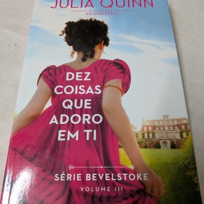 Capa do livro Dez coisas que adoro em ti de Julia Quinn com mulher de vestido rosa e casarão ao fundo