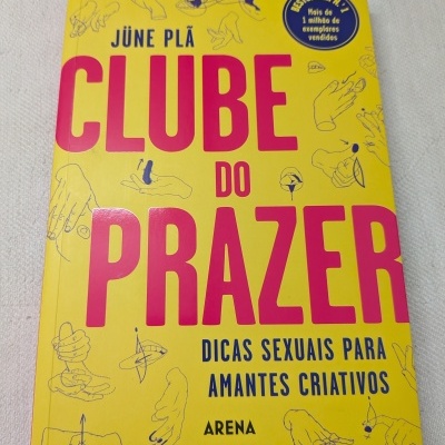 Livro Clube do Prazer com capa amarela, texto rosa e azul e ilustrações de mãos.