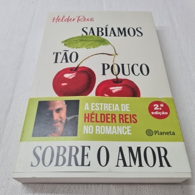 Capa do livro Sabiamos tão pouco sobre o amor com cerejas e faixa promocional do autor Hélder Reis
