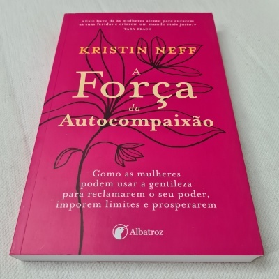 Livro rosa 'A Força da Autocompaixão' de Kristin Neff com desenho de flor e texto branco e amarelo