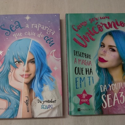 Dois livros coloridos com capa dura, um lilás e outro verde, com imagens de mulher de cabelo azul e títulos em texto brilhante.