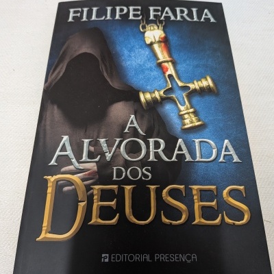 Capa do livro A Alvorada dos Deuses com figura encapuzada e cruz dourada