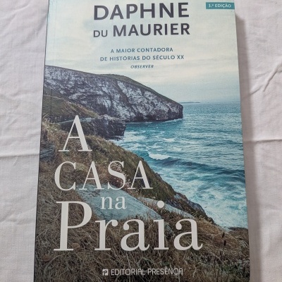 Livro com capa de penhascos e mar, título 'A Casa na Praia'.