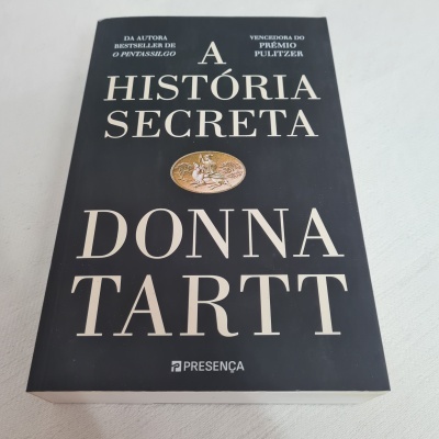 Capa do livro 'A História Secreta' de Donna Tartt, preta com texto branco e imagem oval dourada.