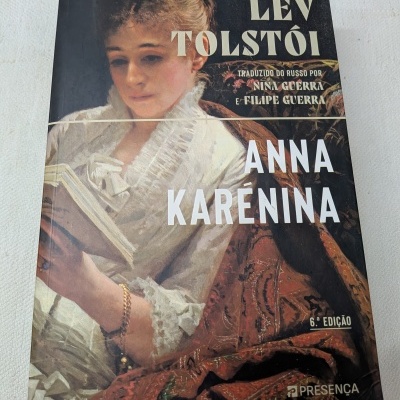 Capa do livro Anna Karénina de Lev Tolstói com pintura de mulher vestindo roupa branca a ler um livro