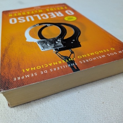 Livro de capa mole laranja com imagem de algemas sobre tecido branco.