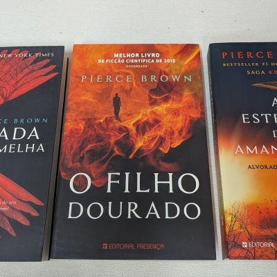 Três livros de Pierce Brown com capas em tons vermelhos e laranja, dispostos em linha sobre fundo branco.