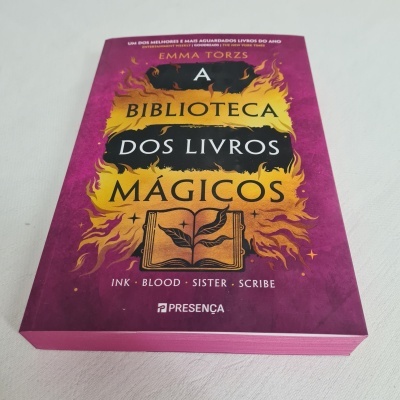 Livro 'A Biblioteca dos Livros Mágicos' com capa roxa decorada com chamas amarelas e pretas