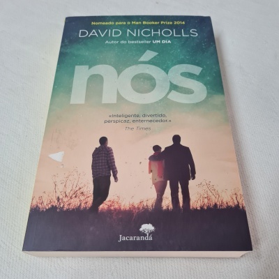 Capa do livro 'nós' de David Nicholls com três silhuetas no campo ao pôr do sol.
