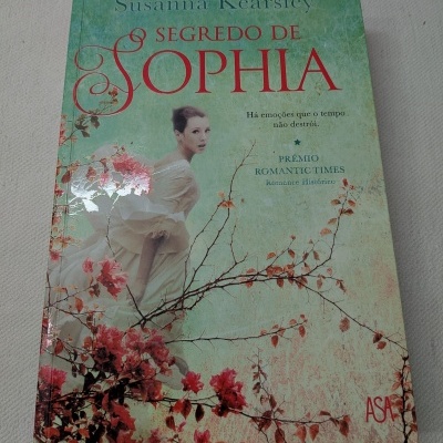 Capa de livro O Segredo de Sophia com mulher de vestido branco e flores vermelhas num fundo verde