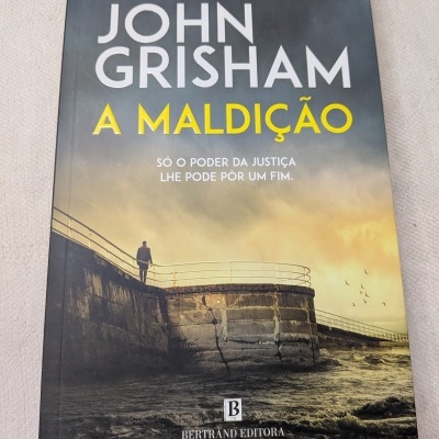 Capa do livro a cores com título A MALDIÇÃO e imagem de cais e mar.