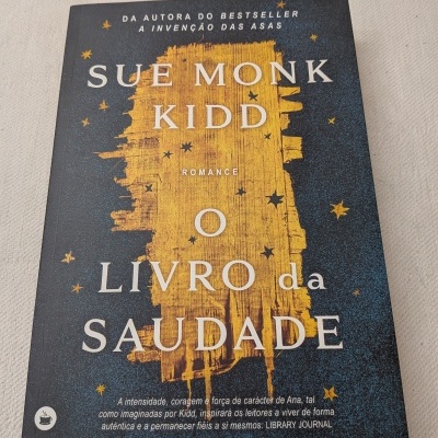 Capa de livro O Livro da Saudade de Sue Monk Kidd com design azul escuro e amarelo e estrelas amarelas